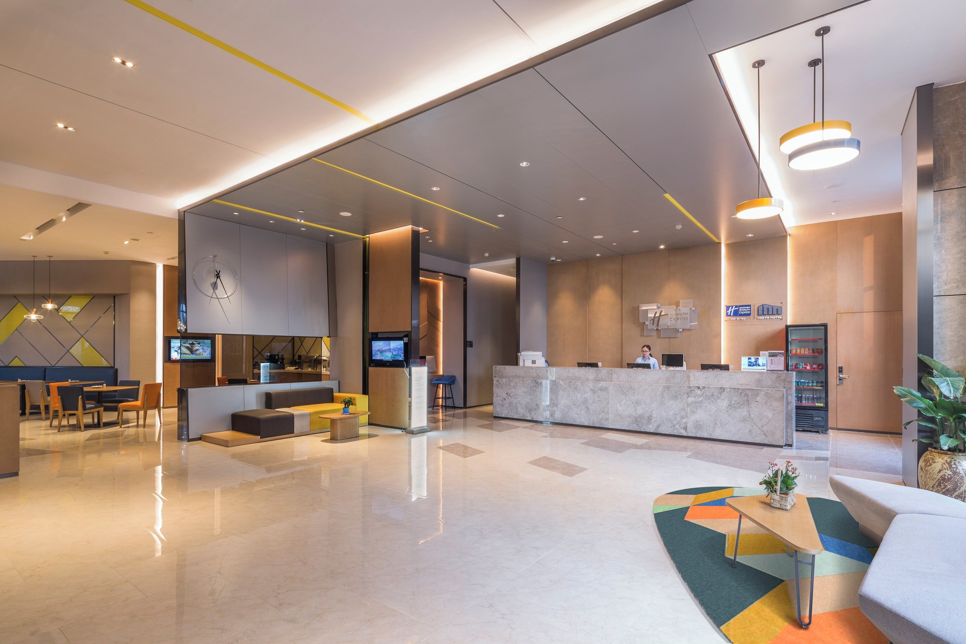 Un moderno vestíbulo de hotel con una recepción, zona de estar y una pantalla de televisión.