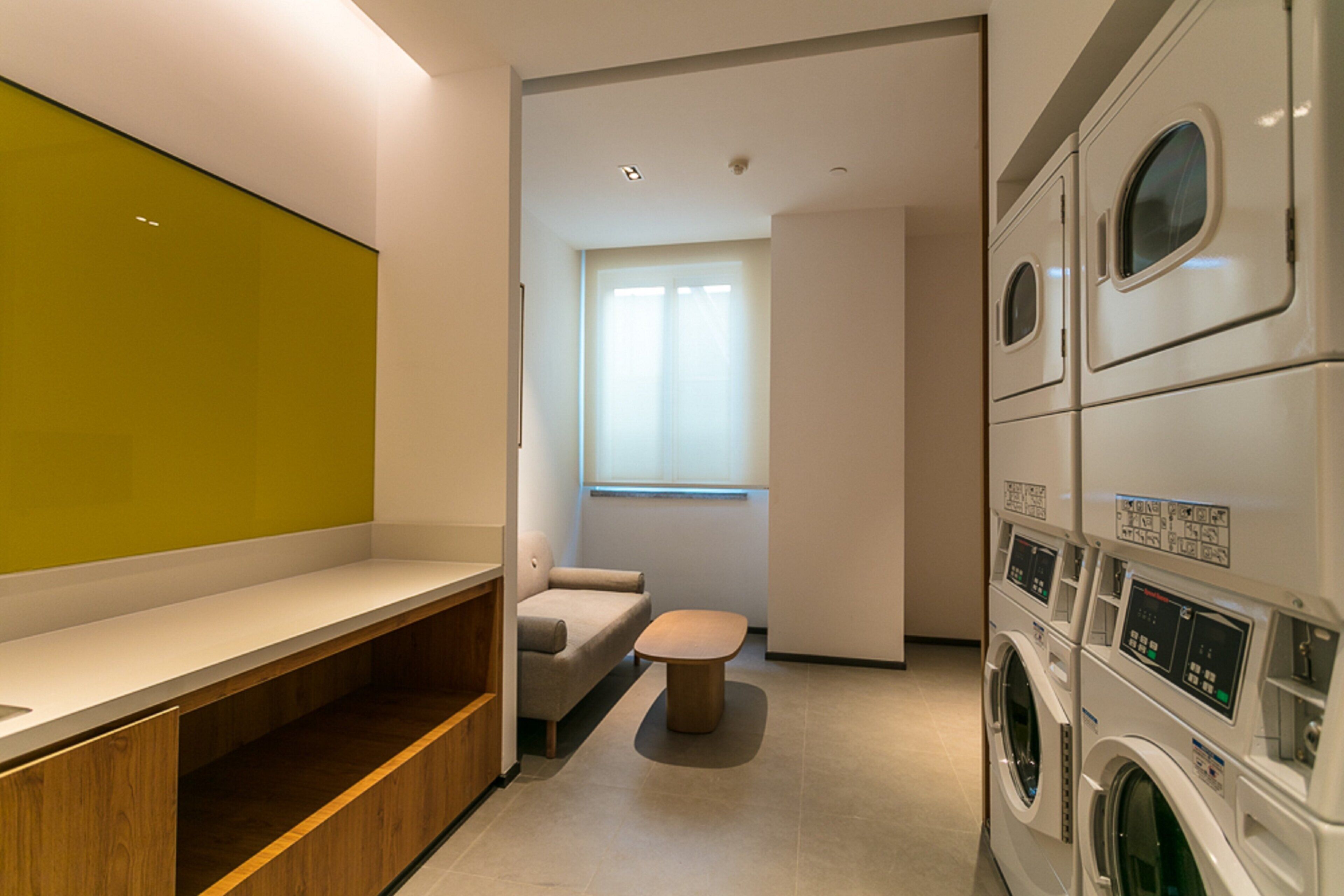 Un moderno lavadero con lavadoras apiladas y una zona de estar con banco y sillón.