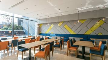 A modern dining area with tables and chairs, large windows, and a geometric wall design.