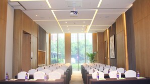 Una sala conferenze con file di sedie e tavoli, un proiettore e ampie finestre che offrono vista sul verde.