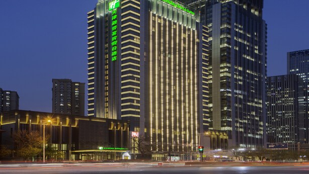 Un hotel moderno de gran altura con líneas verticales y letreros iluminados, rodeado de otros edificios altos.