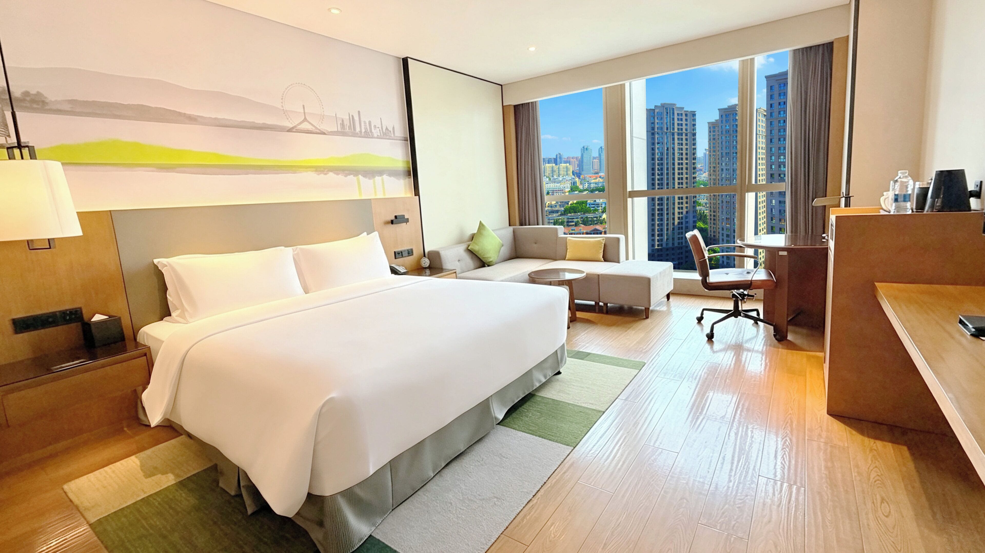Quarto de hotel com uma cama grande, uma escrivaninha, um sofá e vista para edifícios altos.