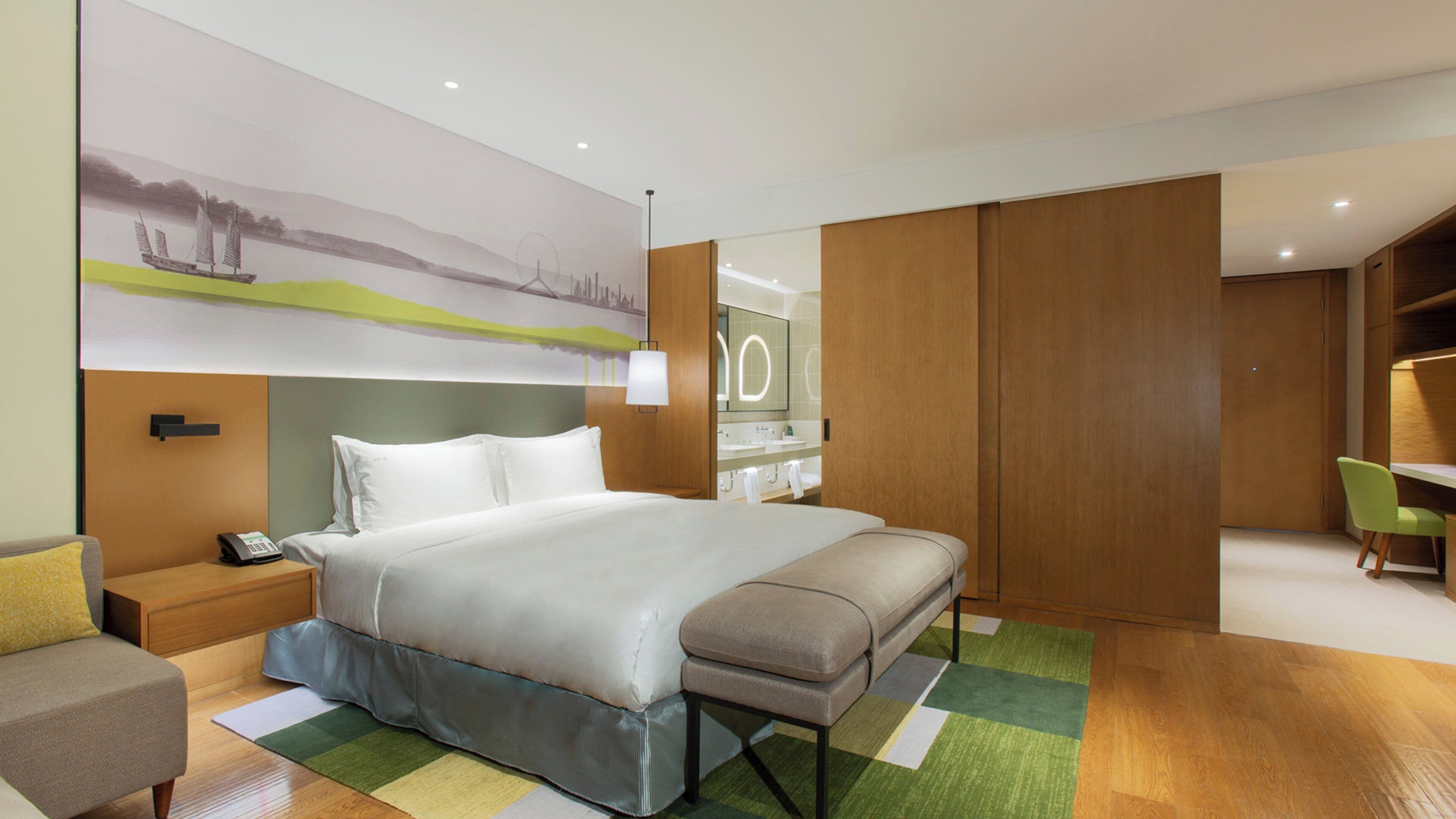 A modern hotel room with a large bed, bedside table, and a desk area.