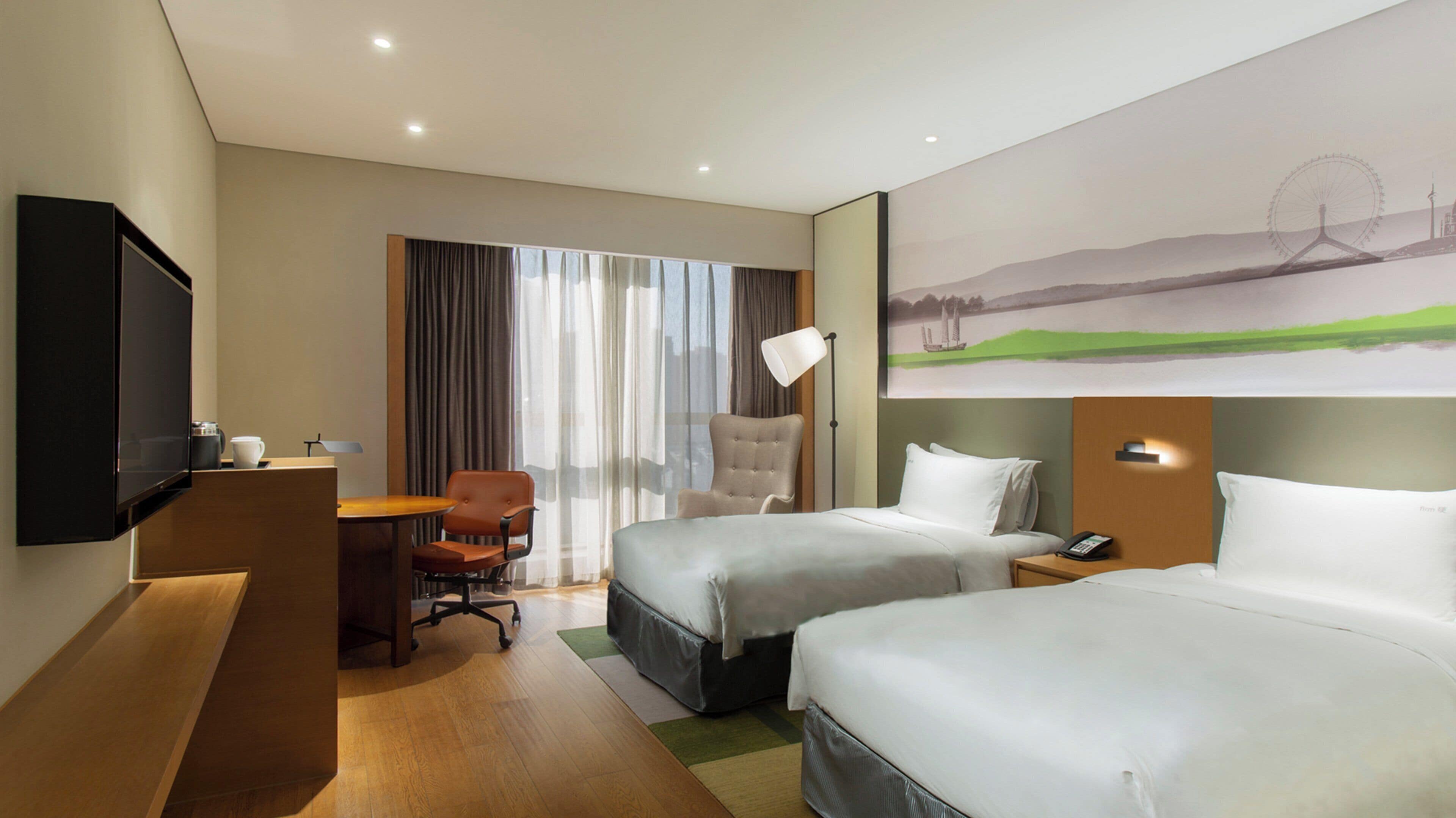 Ein Hotelzimmer mit zwei Betten, einem Schreibtisch, einem Sessel, einem Fernseher und einem Landschaftsbild.
