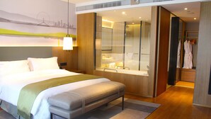 Una camera d'albergo con un letto grande, una panca, un bagno con uno specchio e vista sulla città.