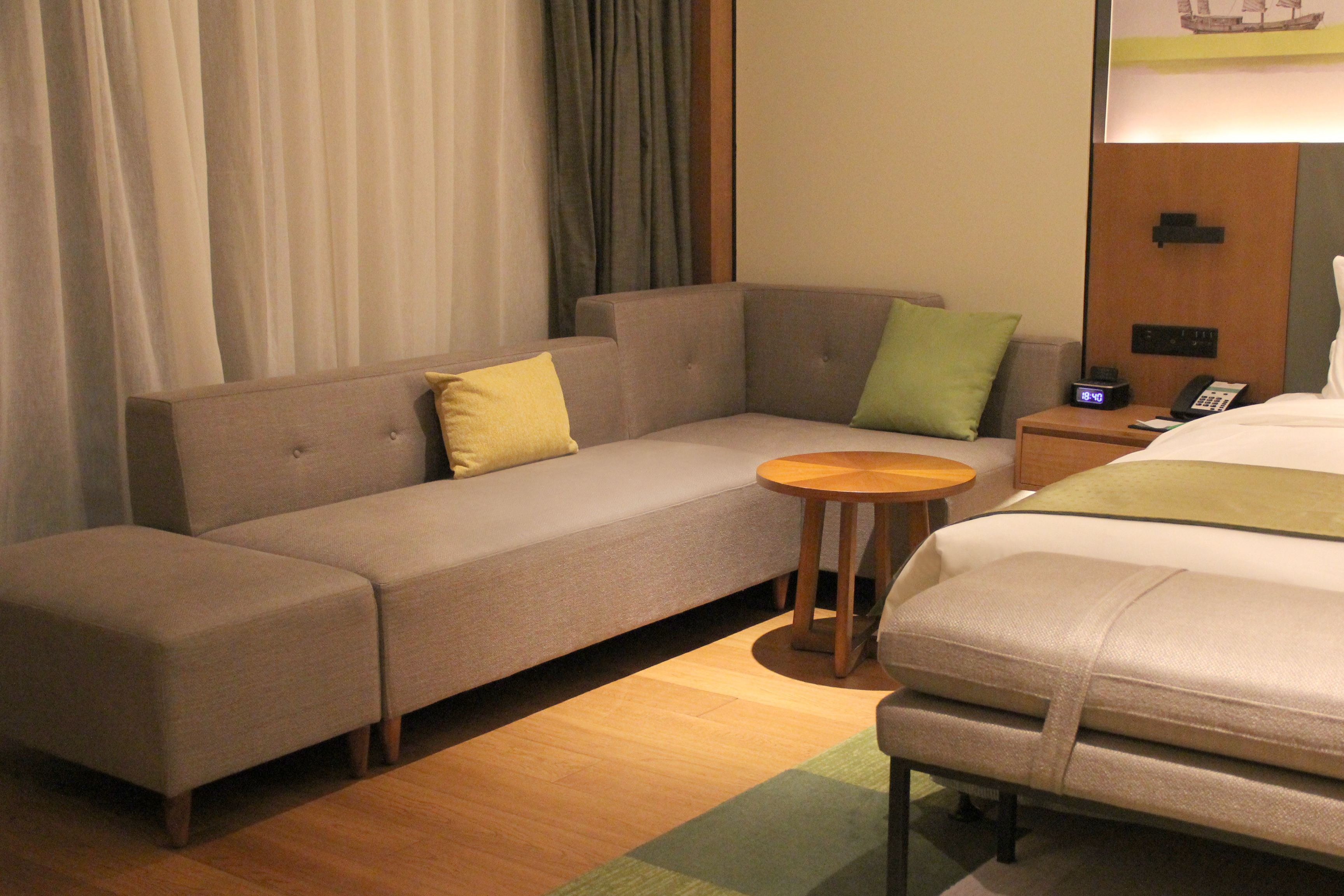 A hotel room with a sofa, a small round table, a bed, and a nightstand with a phone.