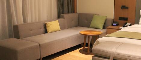 A hotel room with a sofa, a small round table, a bed, and a nightstand with a phone.
