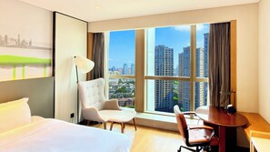 Une chambre d’hôtel équipée d’un lit, d’un bureau, d’une chaise, d’une lampe et d’une grande fenêtre donnant sur la ville.