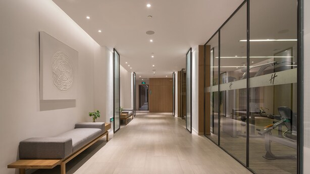 Een moderne hal met een bank, een wandkunstwerk en een glazen wand die fitnessapparatuur weerspiegelt.
