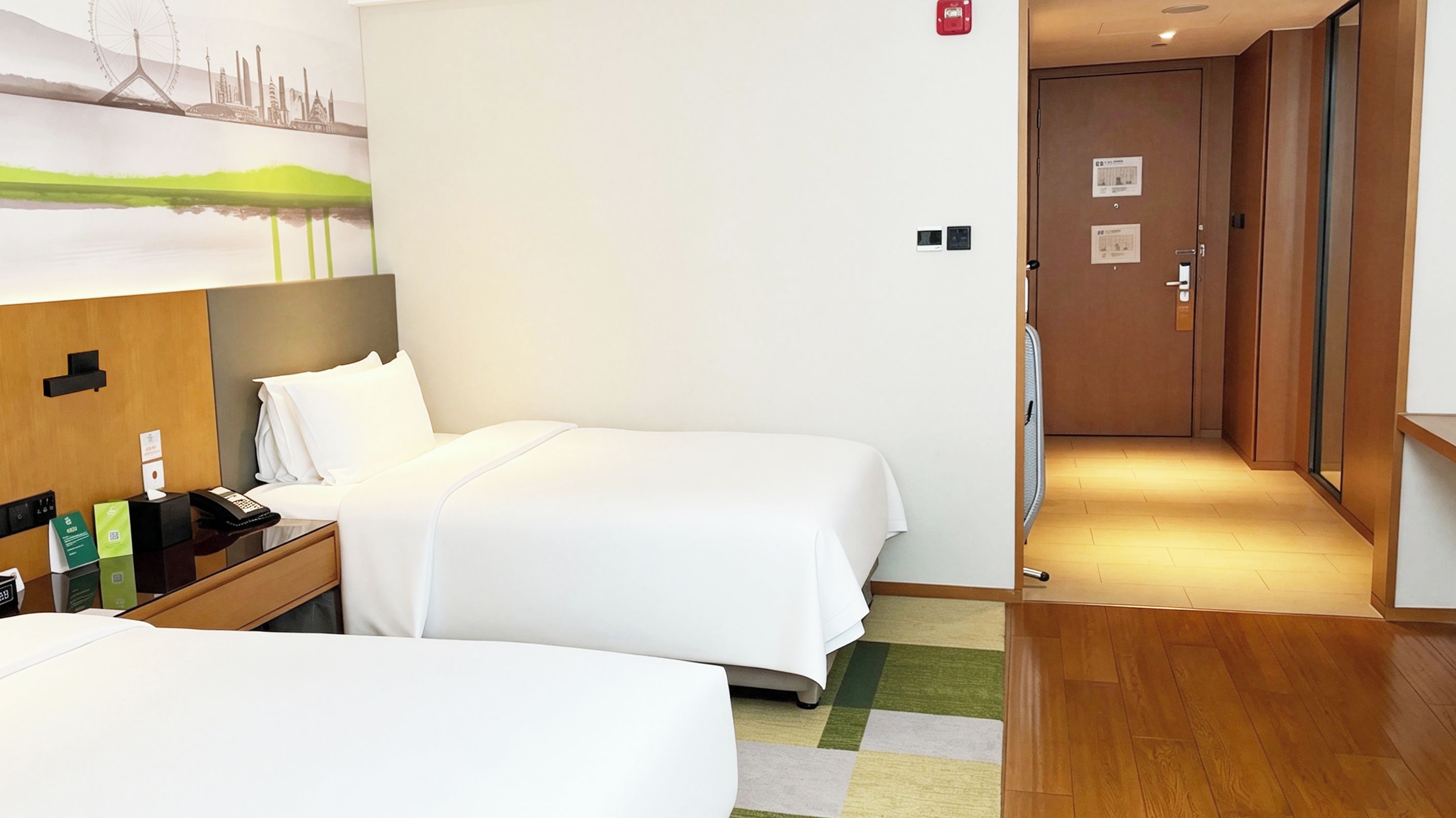 A hotel room with two beds, a desk with a phone and a notepad, a painting on the wall, and a wooden floor.