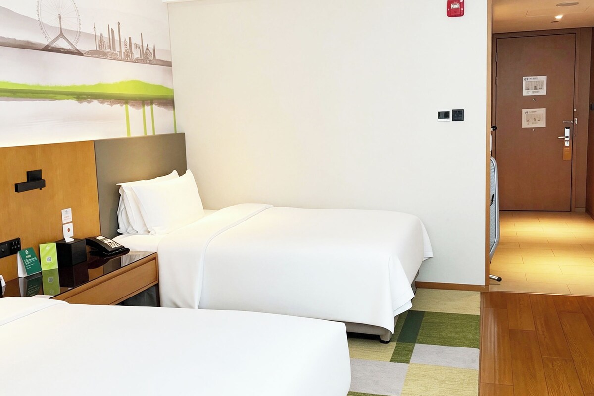 Een hotelkamer met twee bedden, een bureau met telefoon en notitieboekje, een schilderij aan de muur en een houten vloer.