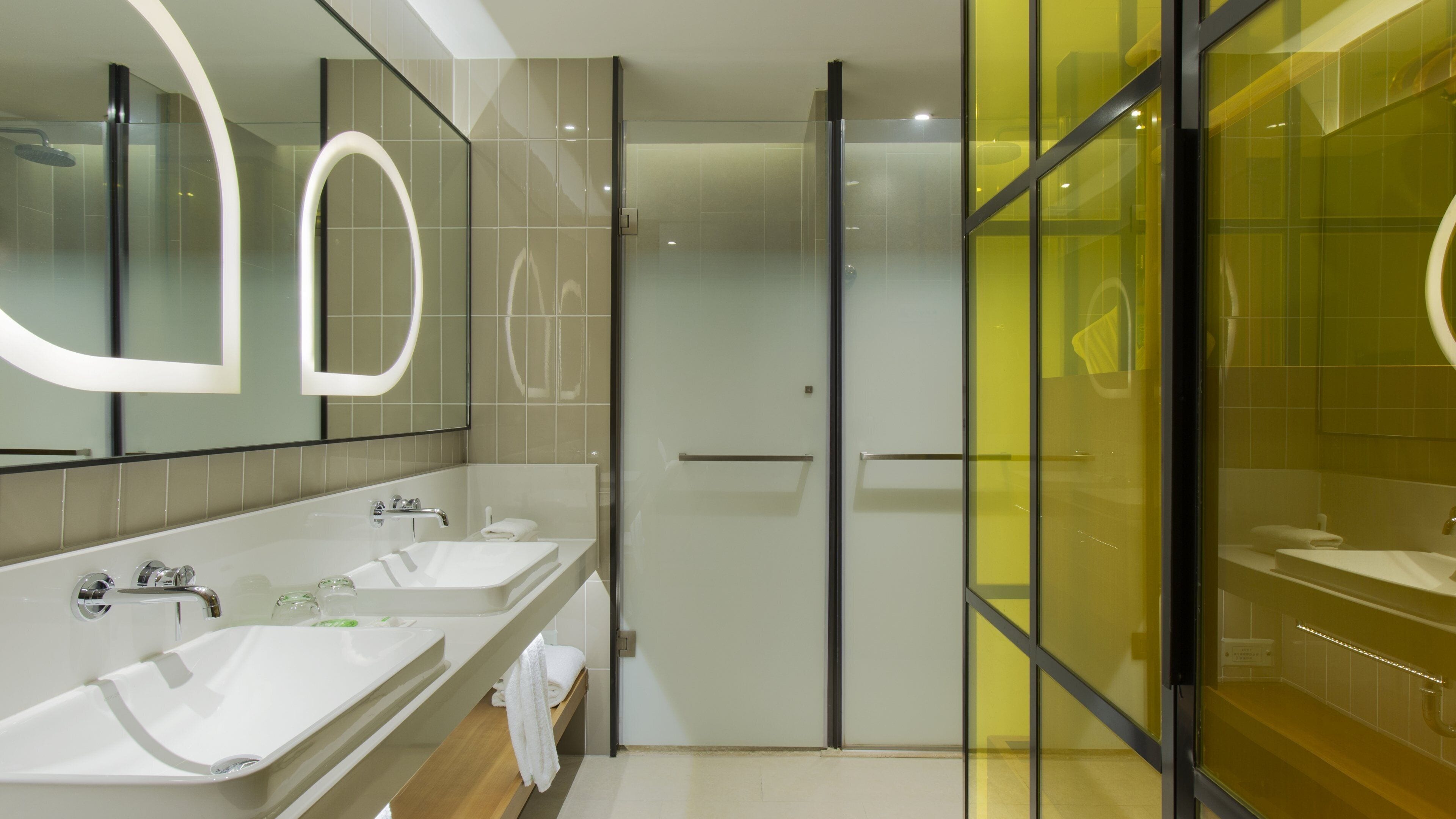 A modern bathroom with two sinks, a glass shower enclosure, and a large mirror with a circular light.