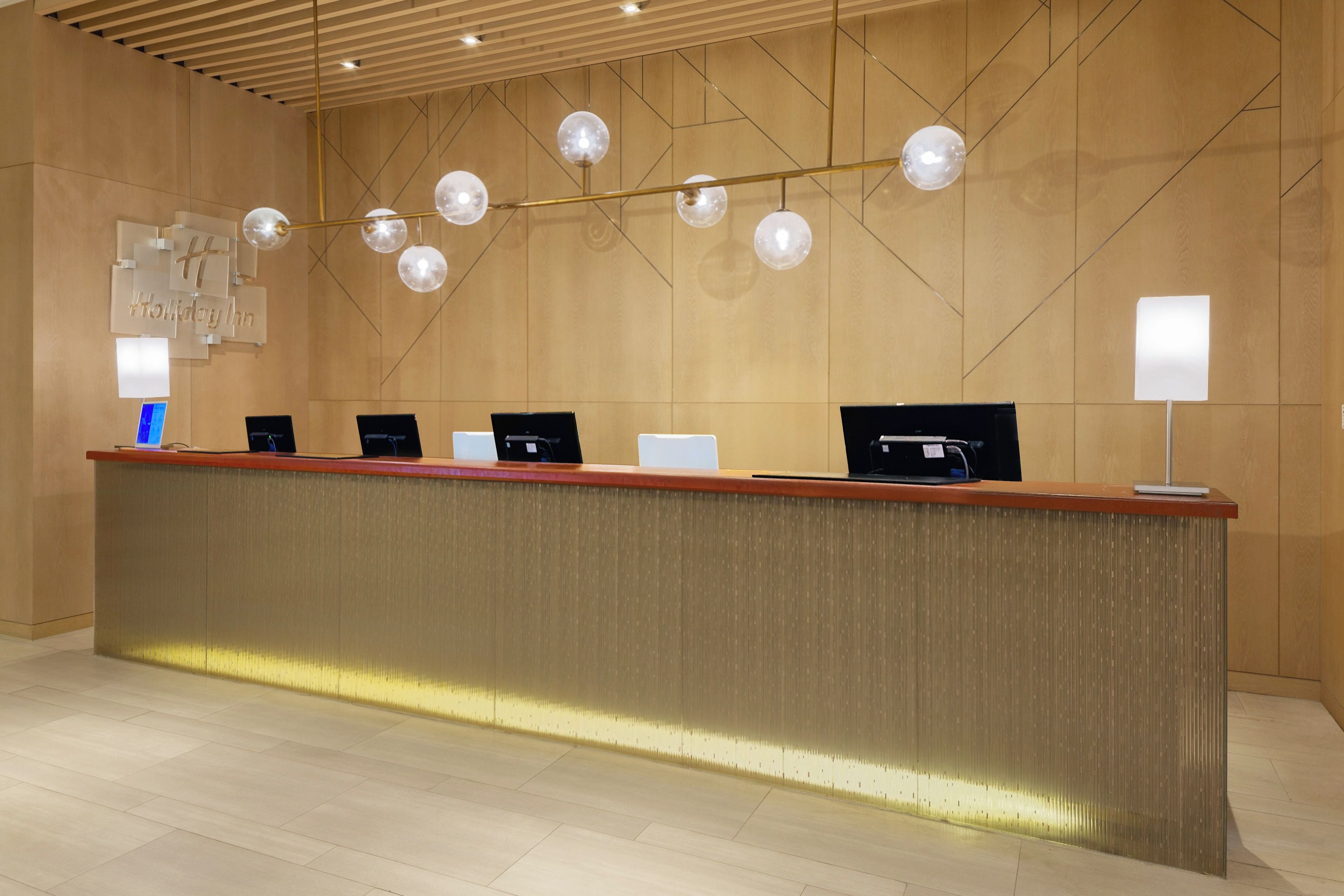 A reception desk with multiple computer monitors, a wooden wall, and pendant lighting.