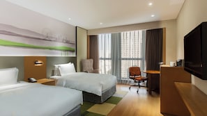 A hotel room with two beds, a desk, a chair, a TV, and a large window with curtains.