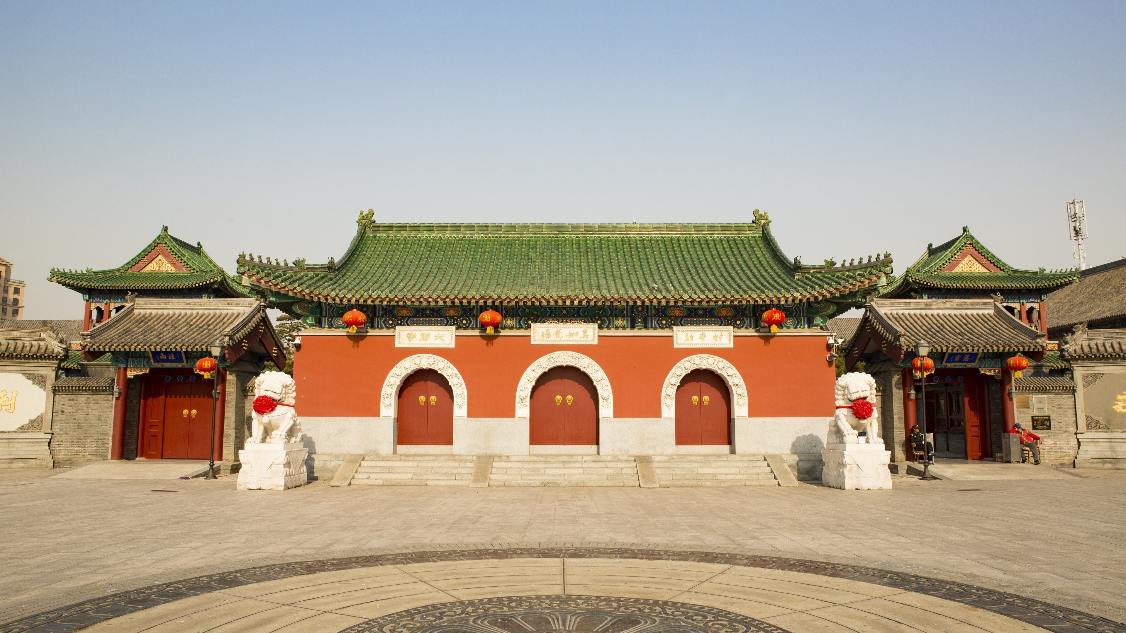 Un edificio tradicional chino con tejado de tejas verdes, puertas rojas y estatuas de leones en la entrada.
