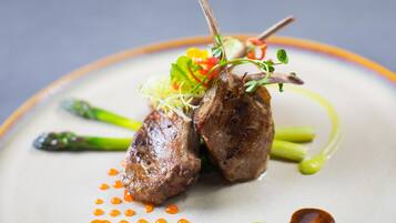A plate of food with asparagus and a piece of meat, possibly lamb, garnished with greens and red peppers.