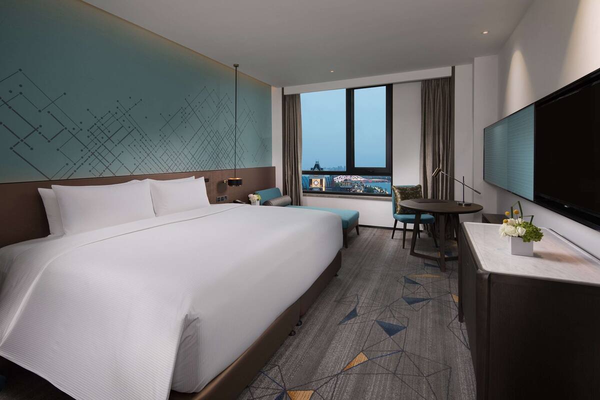 Een hotelkamer met een groot bed, een bureau met een televisie, een zithoek en uitzicht op een stadsbeeld.