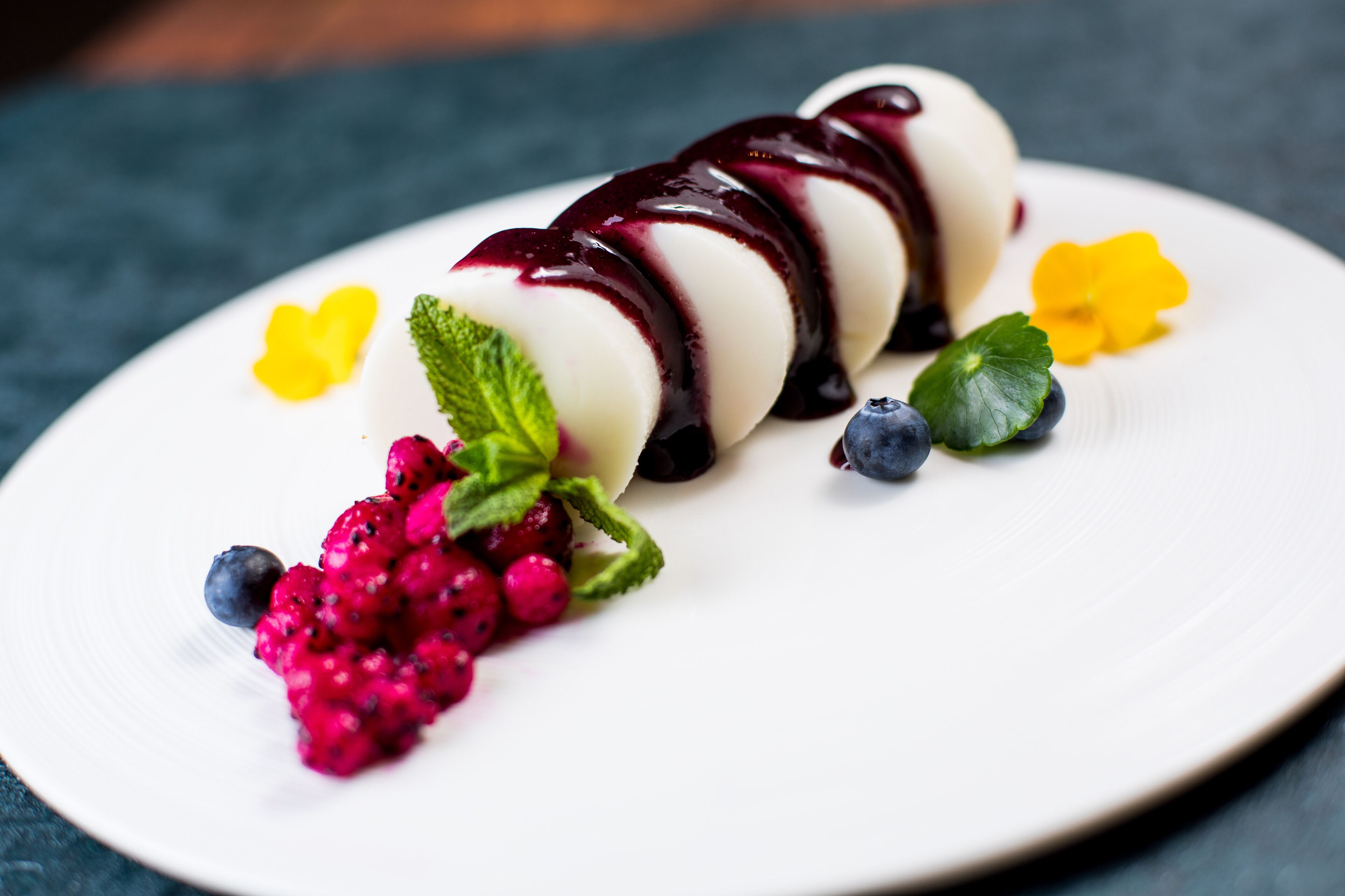 A dessert on a white plate with berries and mint leaves.