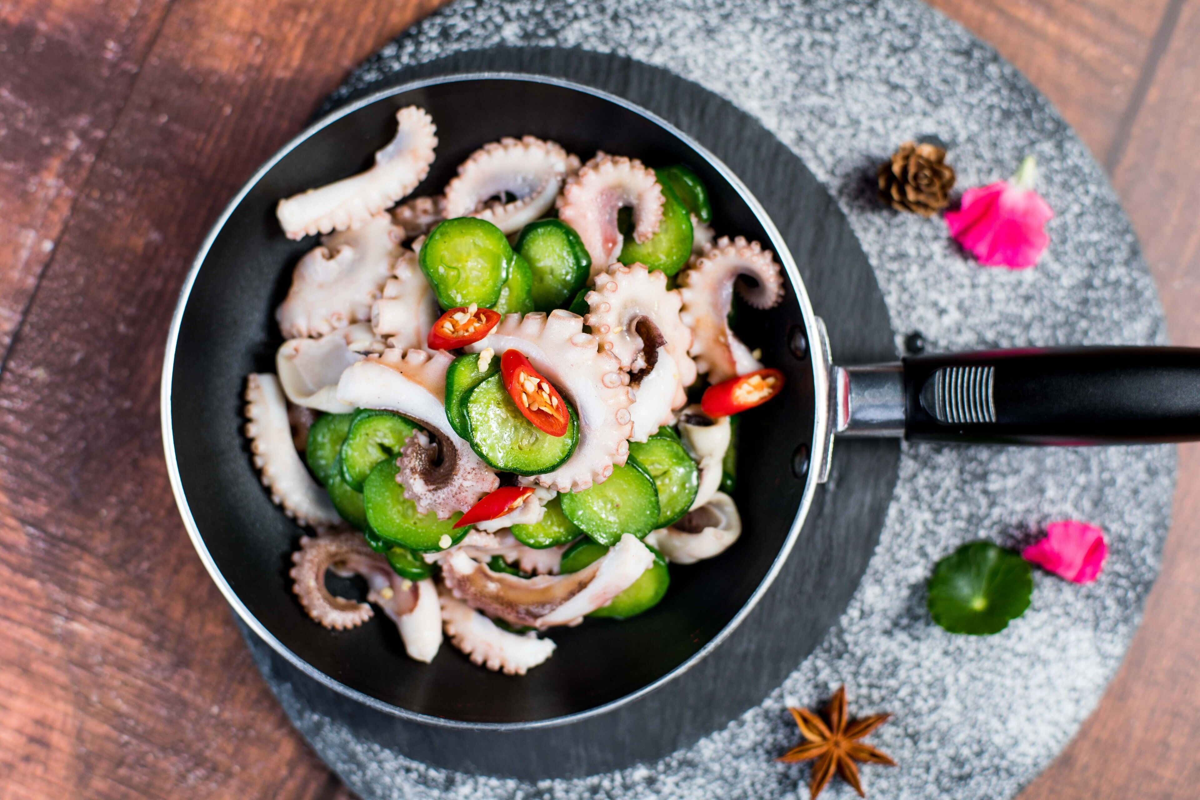 Une poêle contenant des poulpes et des légumes, posée sur une surface en bois.