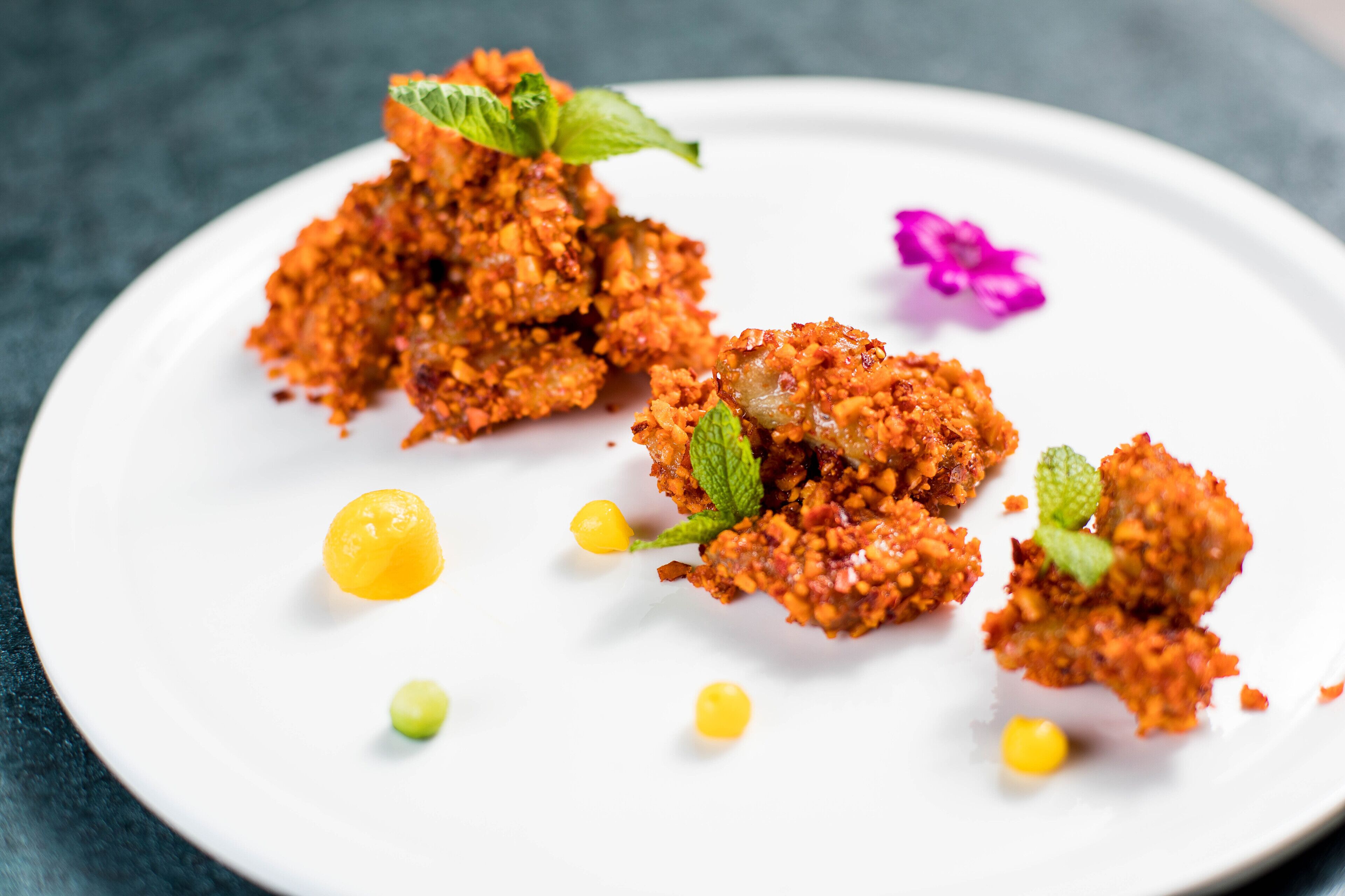 A plate of food with crispy, golden-brown pieces garnished with mint leaves and small yellow and green dots.