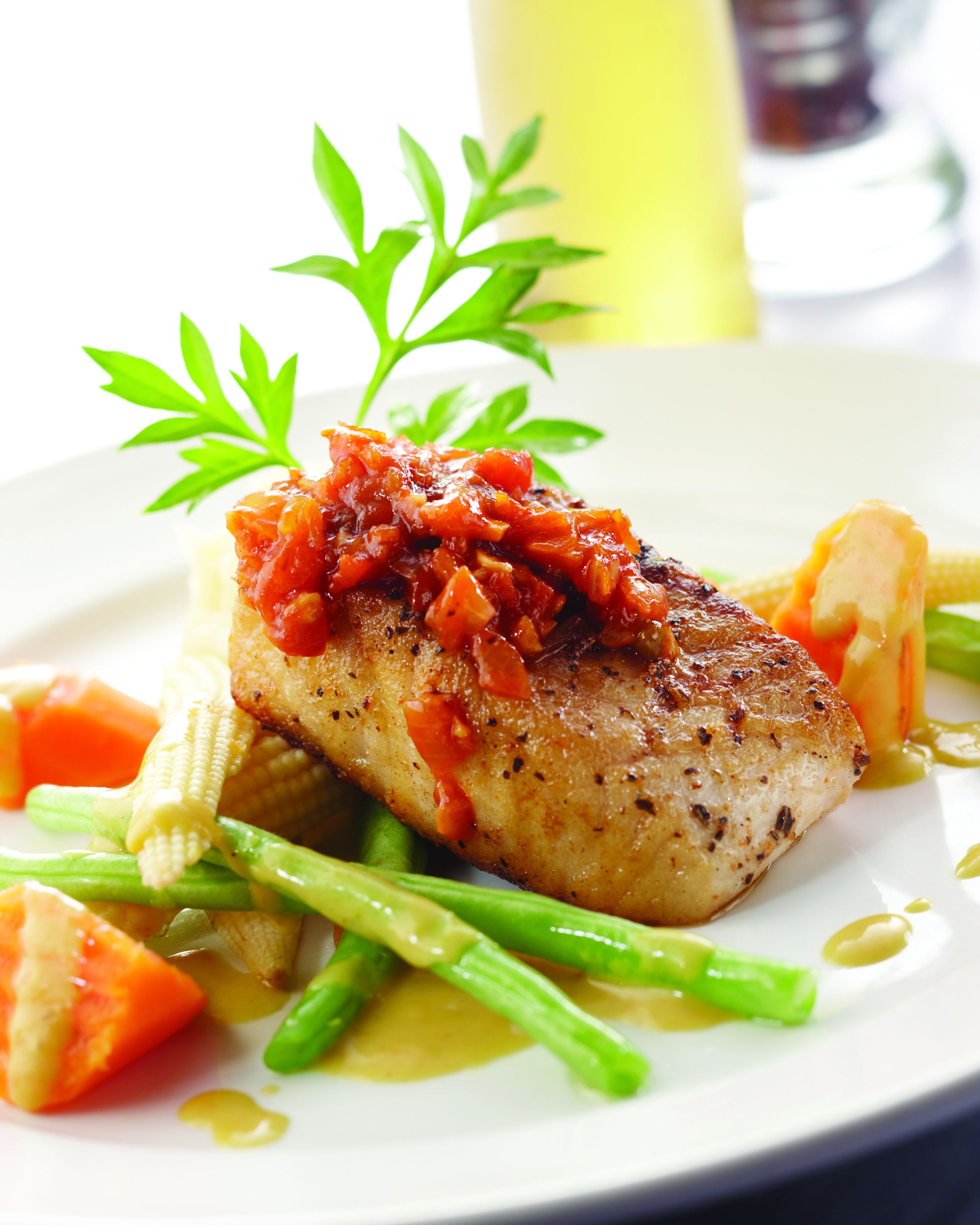 A plate with grilled fish, vegetables, and a garnish.
