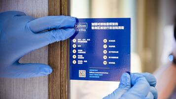A person wearing blue gloves holding a blue card with text and a QR code, likely related to hotel services or information.