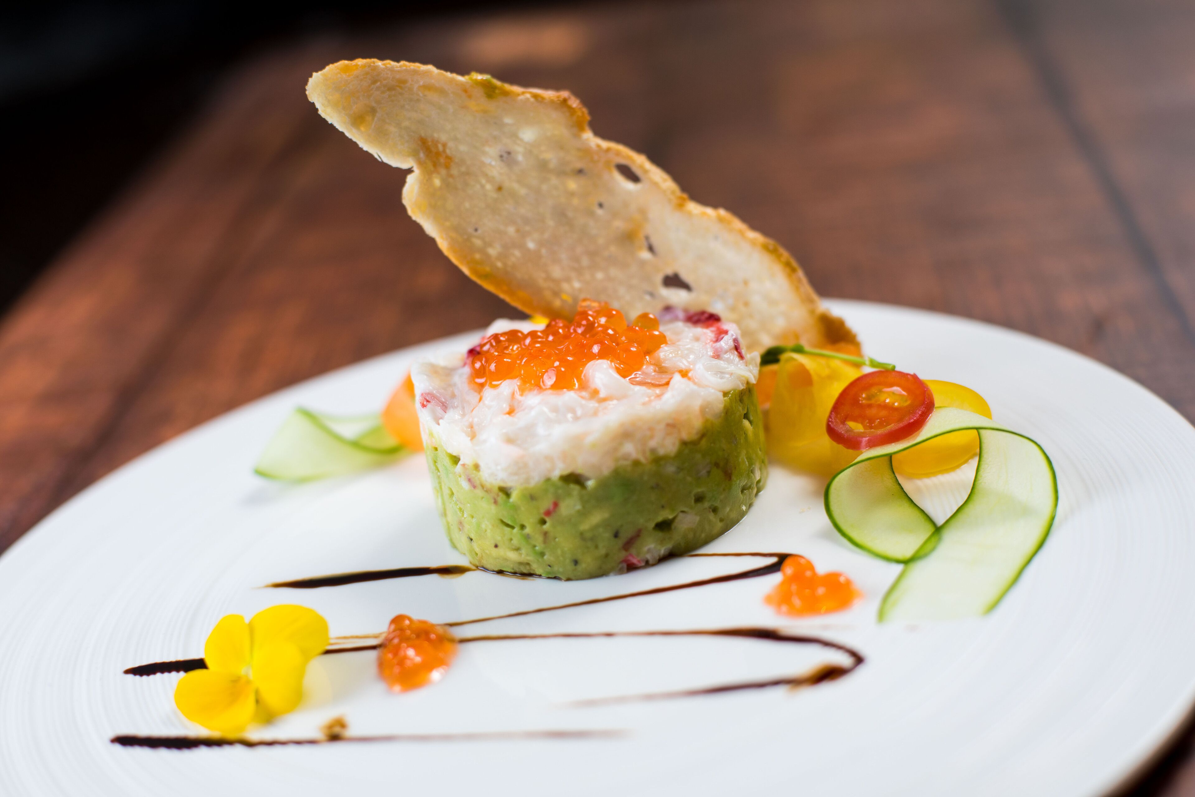 Un plat composé d’avocat, de caviar et de diverses garnitures, présenté sur une assiette blanche.