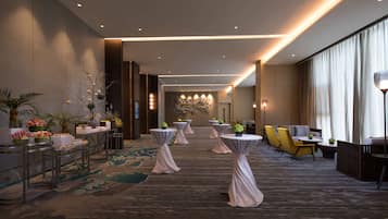 Un amplio vestíbulo de hotel con varias mesas redondas, asientos cómodos y plantas decorativas.