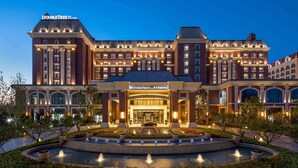 A large, historic hotel with a grand entrance, multiple floors, and a well-maintained garden with a fountain. - DoubleTree by Hilton Qingdao Oriental Movie Metropolis (Qingdao)
