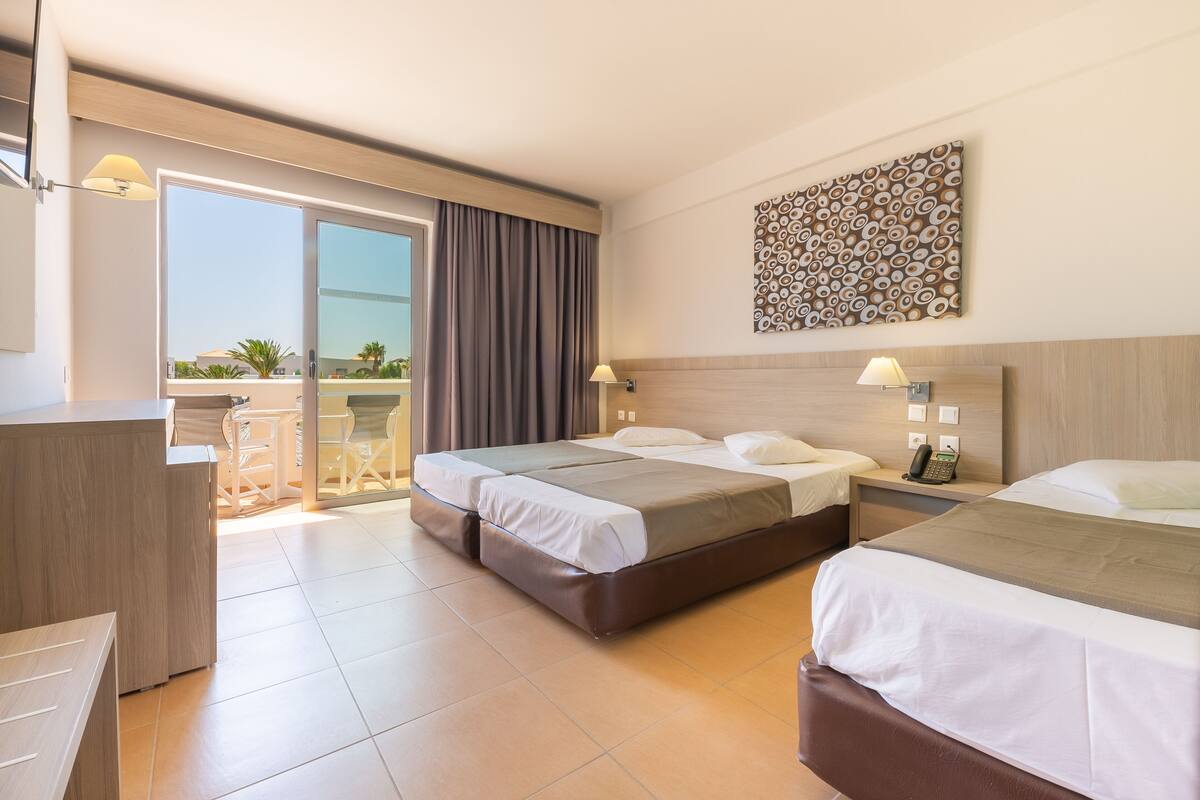 A hotel room with two beds, a desk, and a balcony with a view of the city.