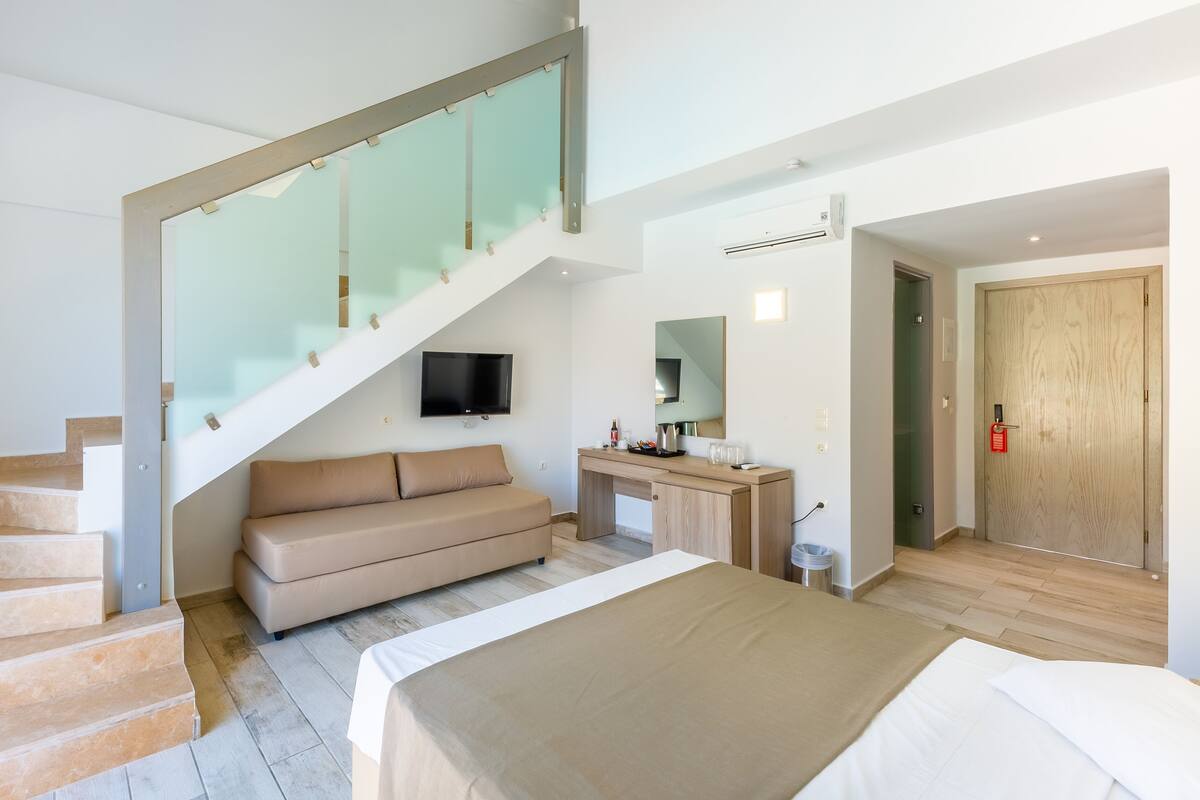 A modern bedroom with a staircase, a sofa, a bed, a desk, and a TV.
