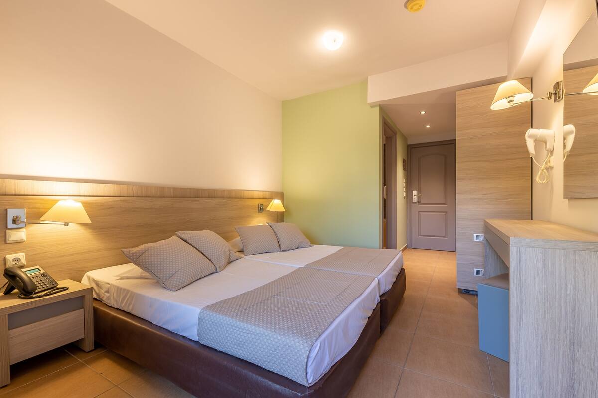 A hotel room with a bed, bedside lamps, a phone on the nightstand, and a desk with a lamp.