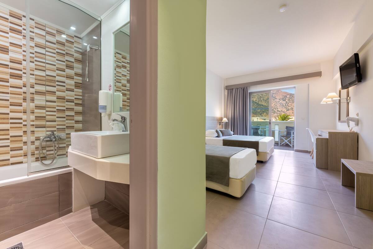 A modern hotel room with a bathroom, a bed, a desk, and a TV.