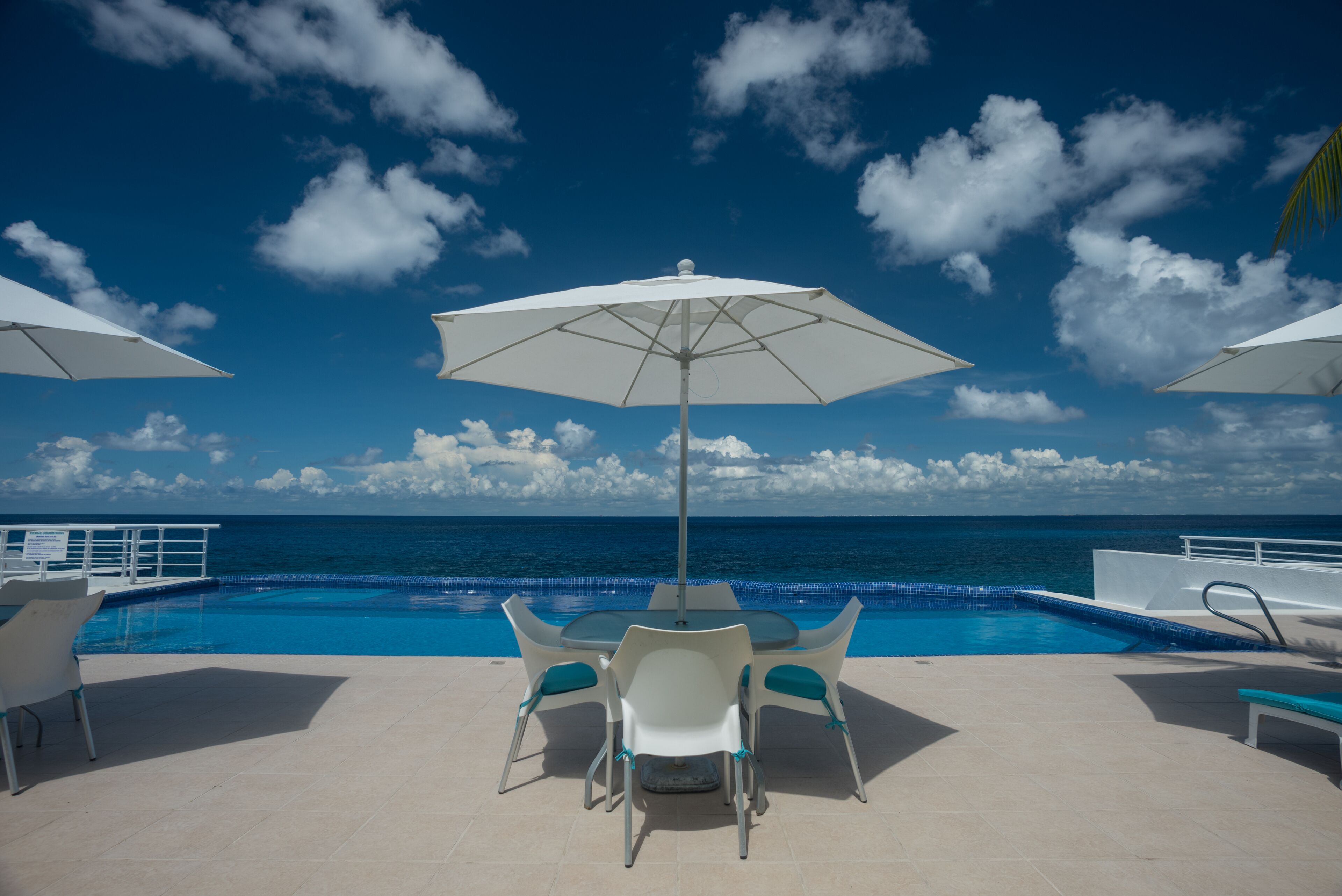 A poolside area with a table and chairs, a large umbrella, and a view of the ocean.