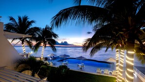 Zona de piscina con sillas de descanso y sombrillas, con vista a un cuerpo de agua al atardecer.