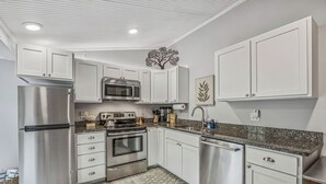A modern kitchen with white cabinets, stainless steel appliances, a granite countertop, and a patterned rug. - Charming Studio Apartment E - Steps to Beach & Dining (Saint Simons Island)