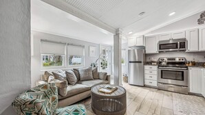 A modern kitchen with white cabinets, stainless steel appliances, and a round wooden coffee table. - Charming Studio Apartment E - Steps to Beach & Dining (Saint Simons Island)