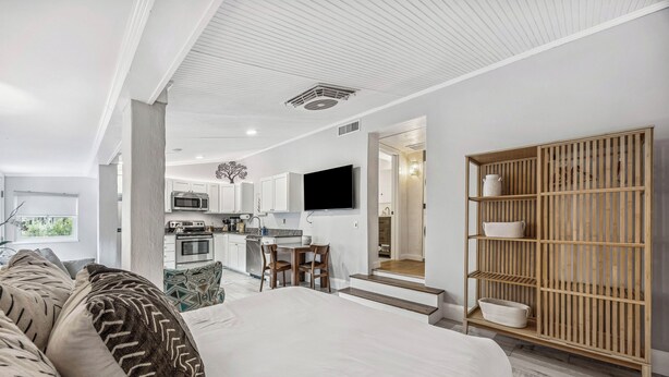 A modern hotel room with a large bed, a wooden sideboard, a kitchen area, and a TV mounted on the wall. - Charming Studio Apartment E - Steps to Beach & Dining (Saint Simons Island)