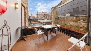 Eine kleine Außenveranda mit Tisch und Stühlen, einem Metallgestell und einer Backsteinmauer.