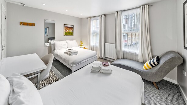 Ein modernes Hotelzimmer mit einem Bett, einem Schreibtisch, einem Sessel und Blick auf die Stadt durch große Fenster.