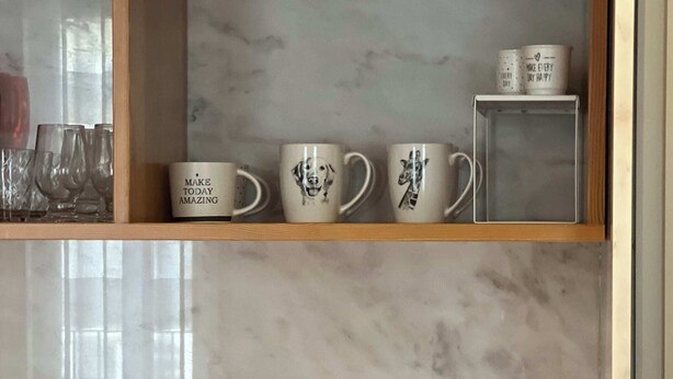 Une cuisine avec un dosseret en marbre, une machine à café, un pot de pâte à tartiner Biscoff et une étagère avec des tasses et des verres.