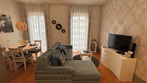 Un salon comprenant un canapé, une table à manger avec des chaises, un téléviseur posé sur un meuble et un papier peint à motifs.