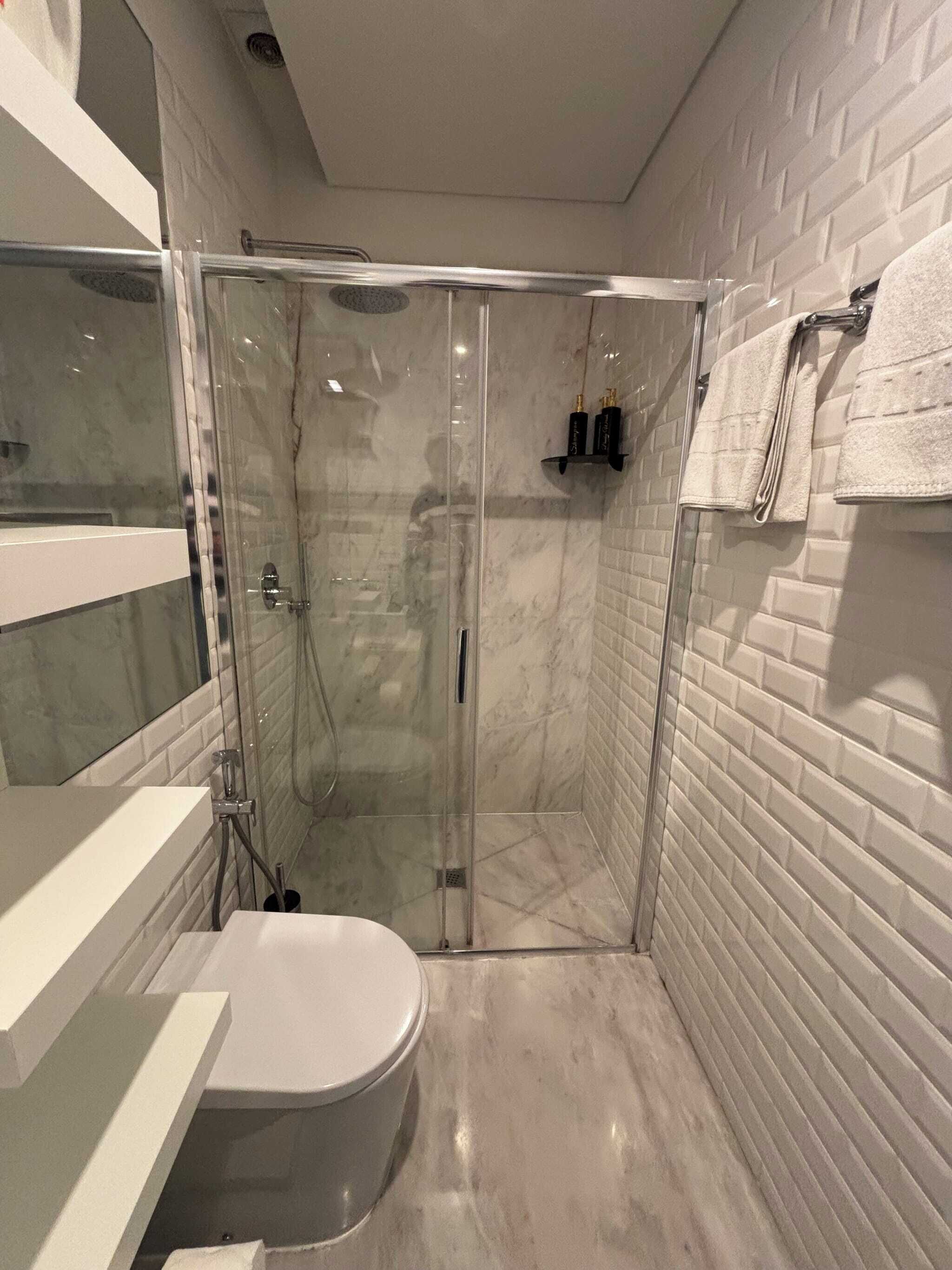 A modern bathroom with a glass-enclosed shower, a white toilet, and a marble-tiled wall.