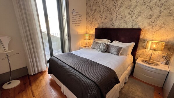 A neatly made bed with a dark headboard, two bedside lamps, and a wall with a quote.