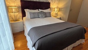 Une chambre avec un grand lit, deux tables de chevet avec des lampes, un mur décoré d’un motif imitant le marbre et un plancher en bois.