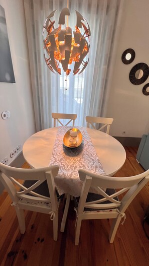 A dining table with a white tablecloth, four white chairs, a chandelier, and a candle holder.