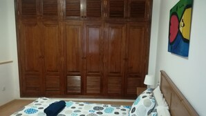 A bedroom with a large wooden wardrobe, a bed with patterned bedding, and a wall painting. - Brisamarina de Órzola (Orzola)