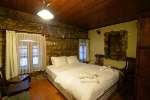 A cozy room with a stone wall, wooden ceiling, a bed with white linens, a chair, and a small table. - Hotel Yorgo Seferis (Urla)