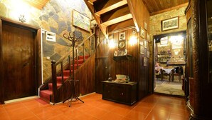 A wooden staircase with red carpet, a coat rack, and a small table with decorative items. - Hotel Yorgo Seferis (Urla)