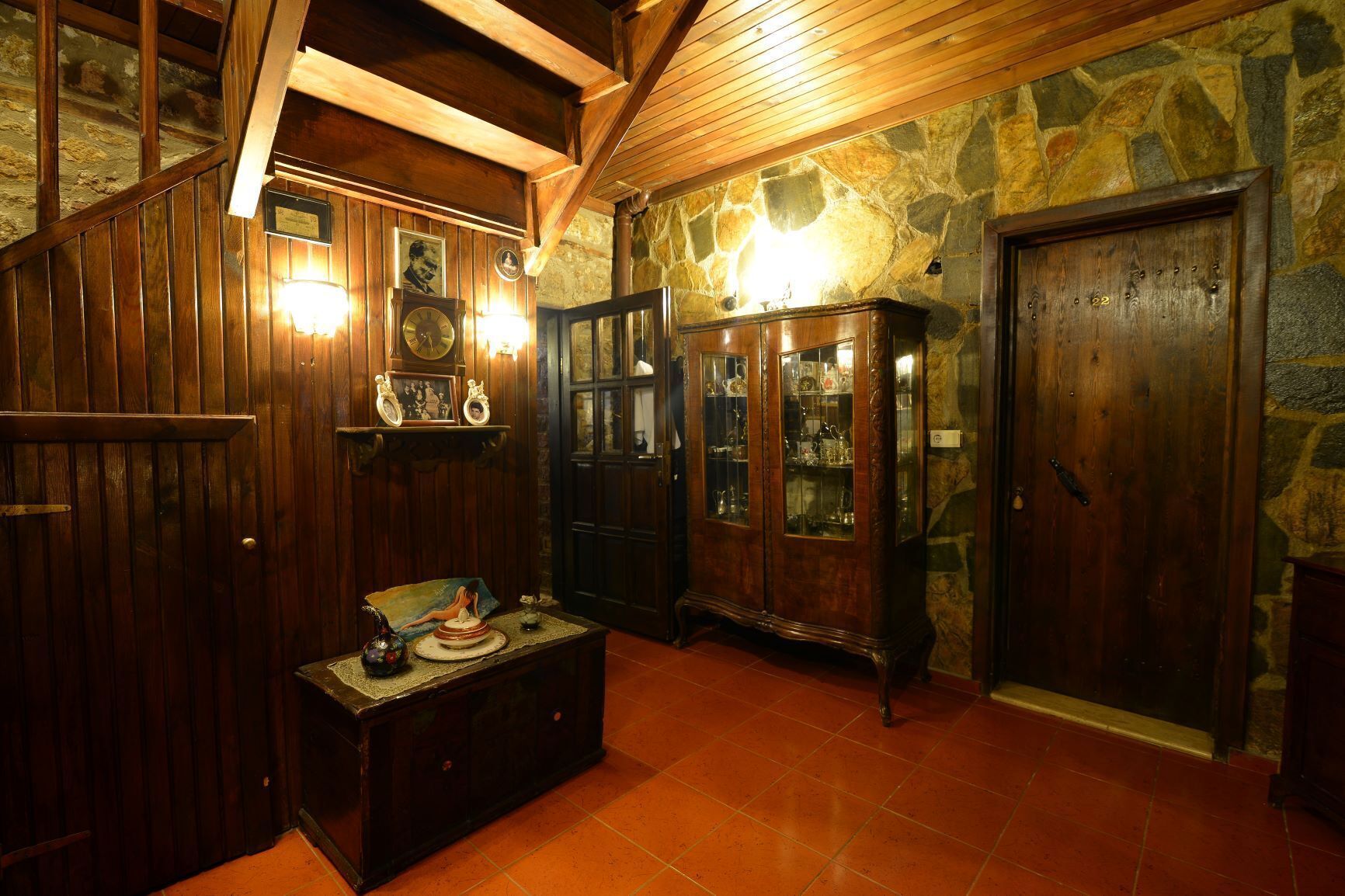 Um quarto com painéis de madeira, parede de pedra, armário de madeira com portas de vidro e piso ladrilhado.